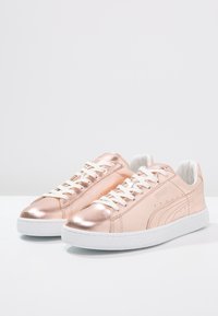 Metallic rosagulliga sneakers med vita snören och gummisålar. Slät textur och minimalistisk design, med subtila logotyp- och sömdetaljer.