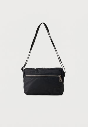 Sort rektangulær crossbody taske med justerbar strop og forreste lynlåslomme på ensfarvet baggrund.