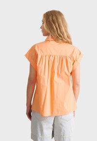 Korte mouwen, oranje shirt met een rugplooidetail, met kraagontwerp en een relaxte pasvorm, gecombineerd met lichtblauwe denimshorts.