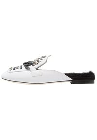 Chaussure blanche à enfiler avec des rivets décoratifs et un dos en fausse fourrure noire. Présente une semelle plate et un design à bout rond.