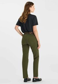 Donkergroene broek met een recht model en een lederen tailleband met luipaardprint, gecombineerd met een zwart shirt met korte mouwen. Zwarte schoenen maken de outfit compleet.