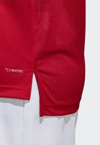 Maglia sportiva rossa con tessuto testurizzato, maniche corte, aperture laterali e logo "Climacool" in bianco sulla parte inferiore sinistra.