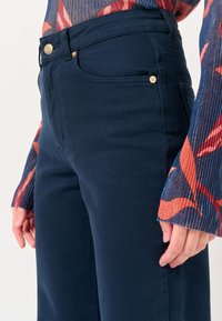 Jeans in denim blu navy con vita aderente, dotati di bottoni dorati, cinque tasche e una finitura pulita con cuciture minime.