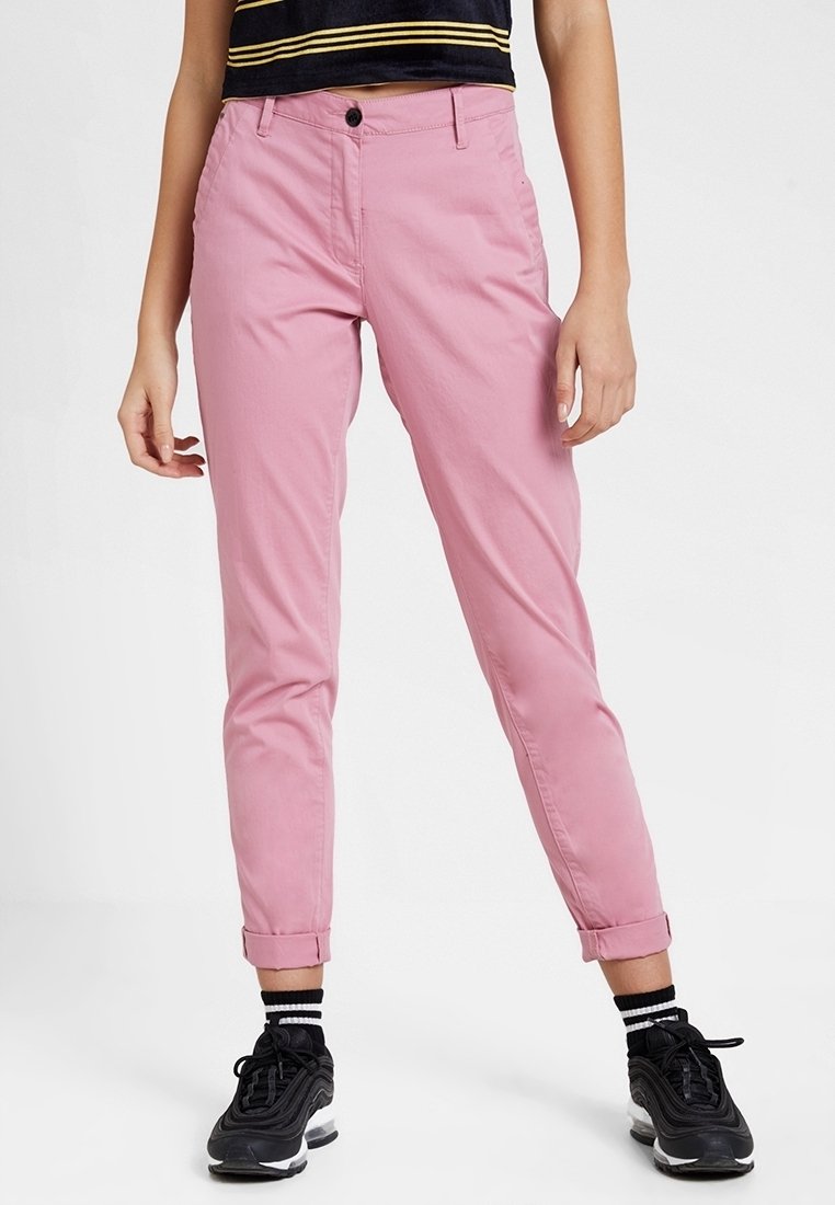 Rosa, avsmalnande chinos med uppvikta ärmslut, tillverkade av bomullsblandat tyg. Har knappstängning fram och sidofickor. Svarta sneakers används.