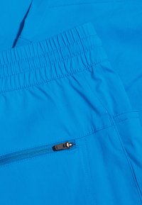 Shorts de sport bleus avec une taille élastique, dotés d'une poche zippée sur le côté et d'une texture de tissu lisse et léger.