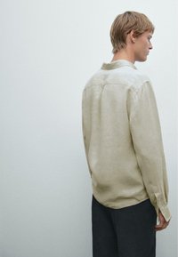 Lys beige linned skjorte med knaplukning ved kraven, lange ærmer og en løs pasform. Bagpå har den en lige ryg og en subtil tekstur.