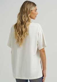 Overdimensioneret hvid bomuldsbluse med korte ærmer, rund halsudskæring og lige kant, der viser en glat tekstur og en afslappet pasform.
