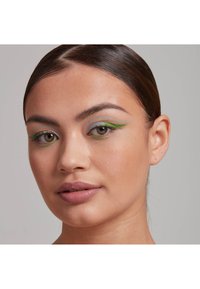 Närbild av ett ansikte med blå och grön eyeliner, neutral läppfärg, slät hudtextur och snyggt bakåtdraget hår.