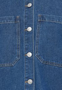 Denim shirt featuring a classic blue color, silver snap buttons, dual front pockets, and contrasting stitching details.