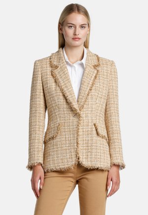 Šviesiai rudos spalvos tweed švarkas su nusidriekusiais kraštais, notch tipo apykakle, dviem priekinėmis kišenėmis ir viena mygtuko uždarymo sistema. Rinkinyje su balta marškinių.