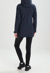 Chaqueta impermeable color navy con capucha, manga larga y diseño entallado. Presenta una textura suave y un sutil detalle del logo en el hombro.