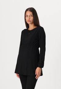 Schwarzes geripptes Still-Tunikakleid mit rundem Ausschnitt und einem Ausschnitt vorne, kombiniert mit schwarzen gerippten Leggings.