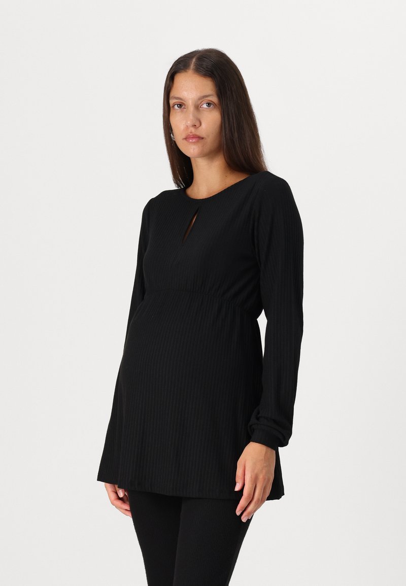 Schwarzes geripptes Still-Tunikakleid mit rundem Ausschnitt und einem Ausschnitt vorne, kombiniert mit schwarzen gerippten Leggings.