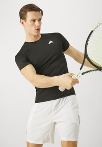 Camiseta atlética negra de manga corta con un logo blanco, combinada con pantalones cortos blancos que tienen bolsillos laterales y detalles en negro.