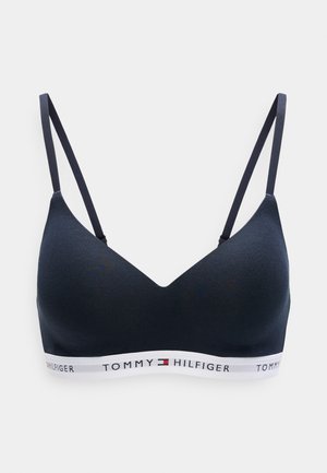 Tamsiai mėlynas vientisas braletas su V formos iškirpte, reguliuojamomis petnešėlėmis ir kontrastinga balta juostele, ant kurios yra raudonos ir mėlynos spalvos prekės ženklas.