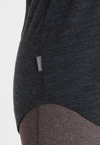 Top atletico nero in un tessuto testurizzato, con un'etichetta logo discreta sul lato. Il design ha una forma aderente, abbinandosi a leggings marroni.