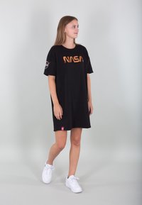 Crna majica haljina s narančastim NASA logotipom, kratkim rukavima i malom crvenom etiketom na rubu. Nosena s bijelim tenisicama.