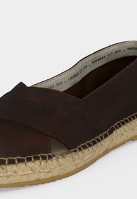 Espadrille marron foncé à enfiler avec des lanières de cuir croisées et une semelle en jute tressée, portant l'inscription "Pavement EST. 2010" à l’intérieur.