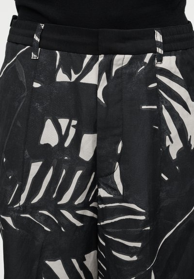 Μαύρο και άσπρο παντελόνι με μεγάλα αφηρημένα φυτικά μοτίβα και φαρδύ μαύρο ζωνάρι στη μέση, συνδυασμένο με μαύρο τοπ.