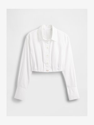 Balts apgrieztais pogāmais krekls ar apkakli, garām piedurknēm un vienu apaļu pogu detaļu apakšējā malā. Gluda tekstūra un viegla auduma.