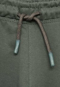 Närbild av midjan på gr�öna tygbyxor med en knuten grå snörning som har blå toppar.