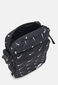 Svart nylonväska med ett upprepat mönster av vita Nike-swooshar, dragkedjestängning och justerbar rem. Kompakt rektangulär design.