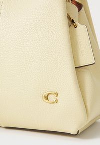 Cream leather handbag featuring a textured surface, gold hardware, and a tag with the brand name. The bag has a structured shape with a rounded base.