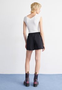 Haut sans manches blanc ajusté avec un décolleté en V, associé à un short noir avec une taille élastique. Bottines noires et roses avec des fermetures éclair.