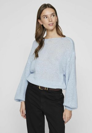 Pull en tricot bleu clair avec des manches larges et amples et un col bateau, associé à un pantalon noir et une ceinture marron. Tissu texturé.
