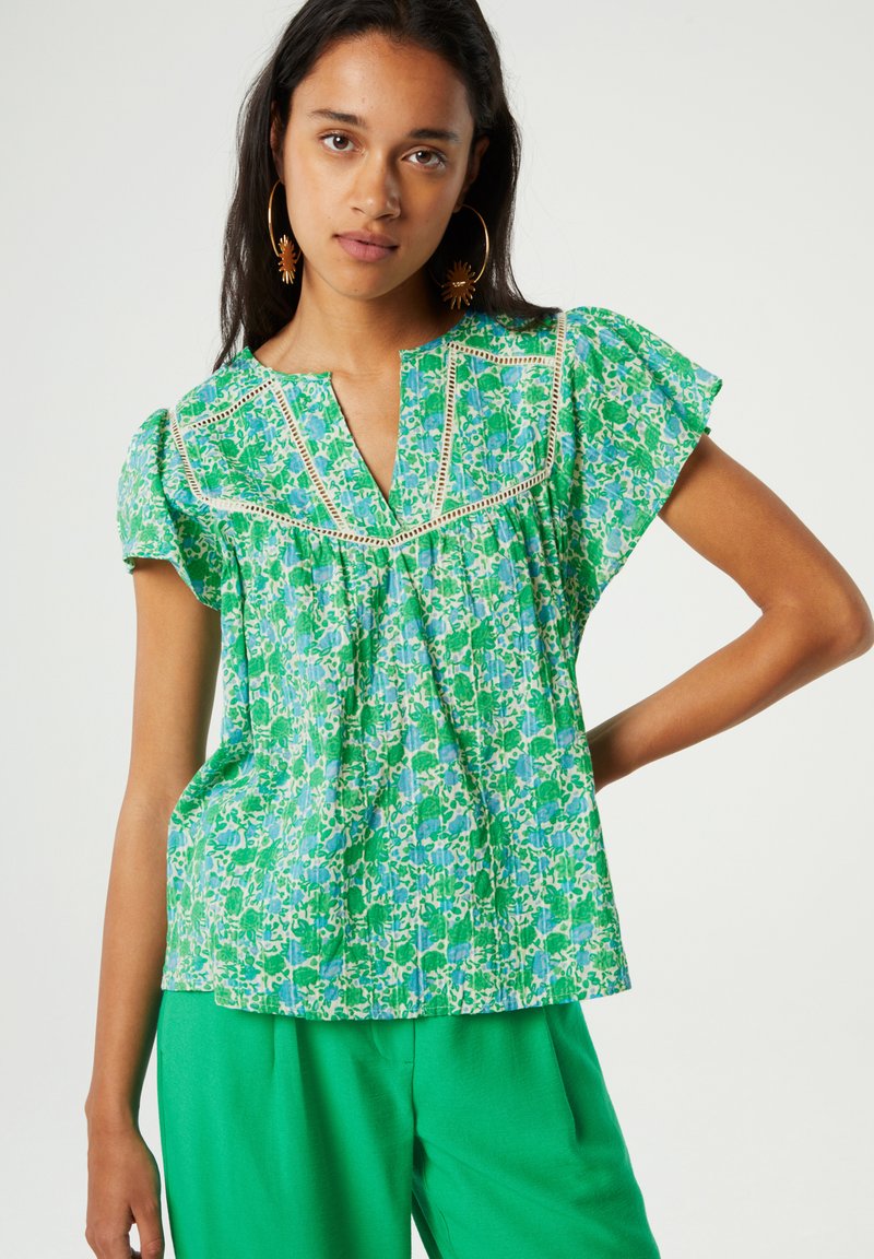 Groene bloemenblouse met korte mouwen, V-hals en geborduurde details. Lichtgewicht stof met een losse pasvorm, gestyled met groene broek.