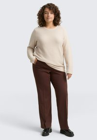 Beige gestructureerde trui met lange mouwen, gecombineerd met taperende donkergroene broeken. Zwarte plateau-schoenen maken de outfit af.