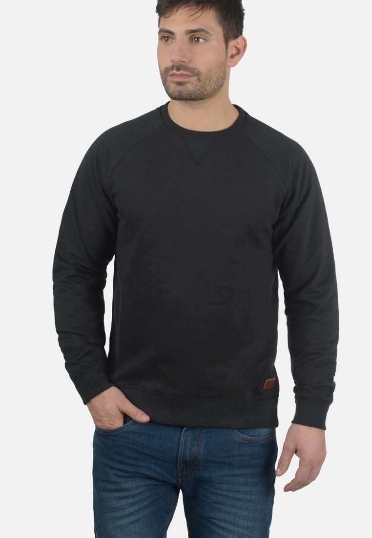 Sweatshirt noir avec des manches raglan, col rond et tissu texturé. Présente une petite étiquette en cuir en bas �à gauche. Assorti avec un jean bleu.