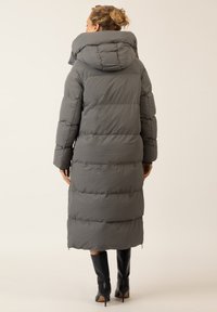 Langer grauer Steppmantel mit hohem Kragen, gestepptem Design und entspanntem Schnitt. Reicht bis zur Mitte der Wade und verfügt über große gepolsterte Abschnitte.