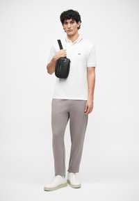 Cămașă polo albă cu logo, pantaloni gri tapered și adidași albi. Geantă crossbody neagră, design simplu, suprafață texturată, curea ajustabilă.