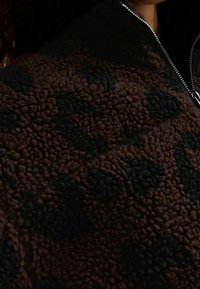 Pullover in pile marrone con collo alto e zip a metà, caratterizzato da un motivo testurizzato in tonalità più scure e una superficie morbida.