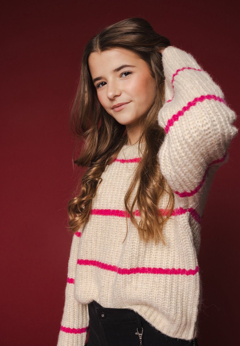 Crème gebreide trui met roze strepen, oversized pasvorm, textuurgaren en geribbelde manchetten, gecombineerd met zwarte high-waisted broek.