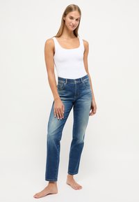 Jeansy z wysokim stanem w odcieniu wyblakłego niebieskiego, wykonane z denimu, z prostą nogawką i pięcioma kieszeniami. Modelka ma na sobie biały top.