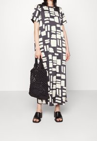 Vestido midi de estampado en blanco y negro con mangas cortas, combinado con un bolso de mano de crochet negro y sandalias de tacón cuadrado negro.