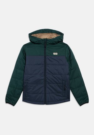 Giubbotto imbottito con cappuccio in verde scuro e blu navy con design trapuntato, cerniera frontale e tasche laterali. Presenta una toppa del marchio sul petto.