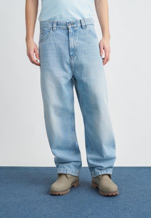 Light blue denim jeans with a relaxed fit, five-pocket design, and a button closure, paired with gray boots on a blue carpet.