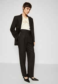 Svart skreddersydd blazer og høyt midje bukser kombinert med en beige topp, som har en knute detalj. Svart spiss tå hæler fullfører antrekket.