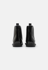 Bottes de cheville en cuir verni noir avec une finition brillante, des panneaux latéraux élastiques et des languettes de tirage. Elles présentent une semelle en caoutchouc plate et une forme simplifiée.