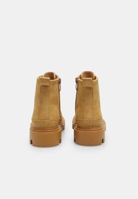 Bottines en cuir tan avec une texture lisse, fermeture éclair et semelles en caoutchouc robustes. Présente une pointe arrondie et des coutures renforcées.