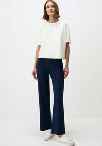 Witte top met korte mouwen gecombineerd met marineblauwe wijde broek en witte sneakers. De top heeft een ontspannen pasvorm; de broek heeft een gladde textuur en wijde benen.