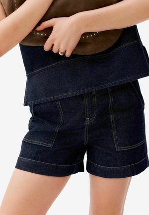 Shorts en denim foncé avec des coutures jaunes, une coupe décontractée et deux poches latérales. La taille est terminée par un ourlet soigné.