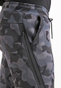 Cargo byxor med ett geometriskt camouflagemönster i grå nyanser. Har en sidoficka med dragkedja, dragsko i midjan och en mjuk tygtextur.