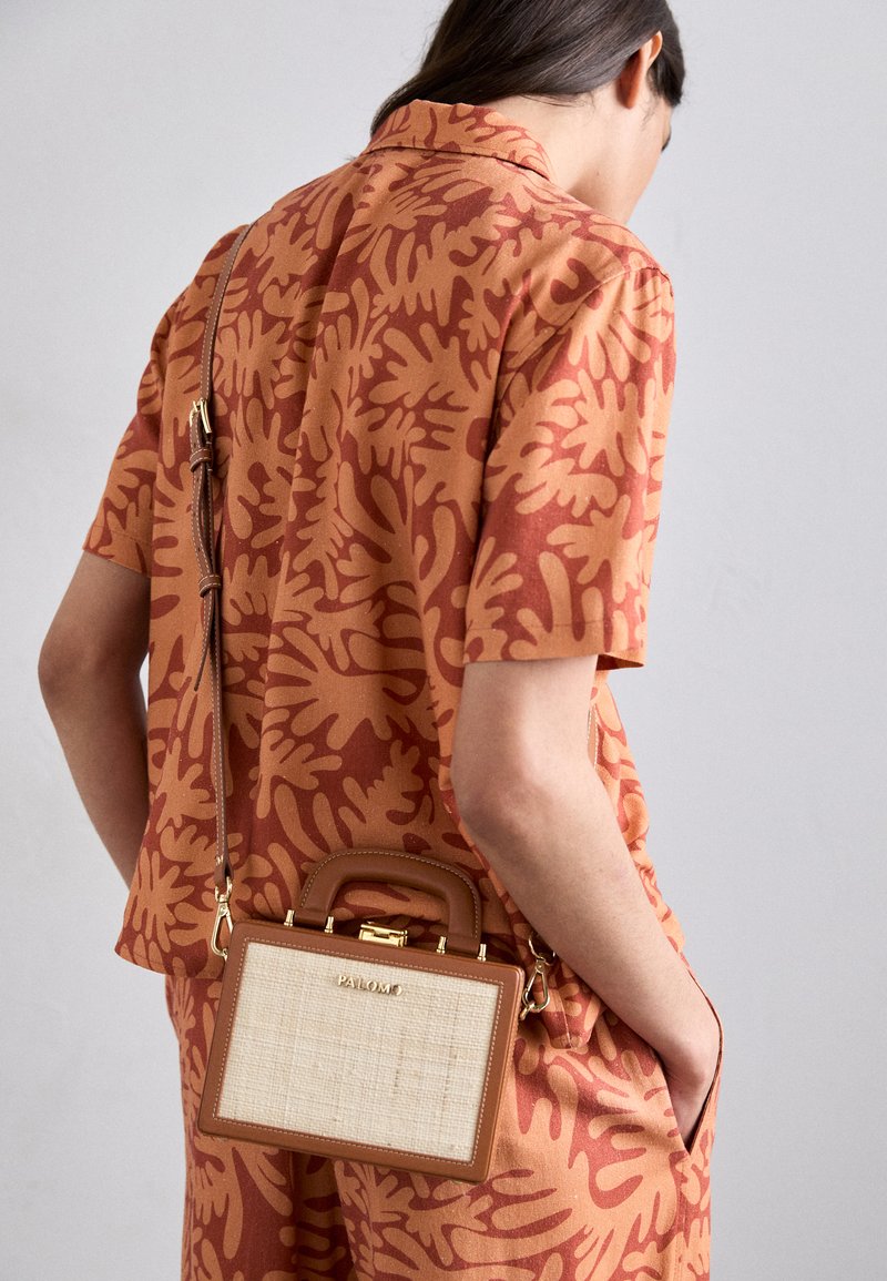 Tan handbag with a textured cream front, gold hardware, and a brown strap. Worn crossbody, paired with a coral patterned shirt.