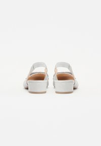 Chaussures slingback en suède gris avec un petit talon bloc, dotées d'un design simple et d'un dos ouvert, mettant en valeur une texture lisse et des accents minimalistes.