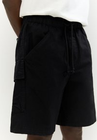 Sorte cargoshorts lavet af stof med elastisk talje, justerbar snor, sidelommer og en struktureret overflade.