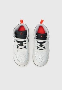 Λευκά δερμάτινα αθλητικά παπούτσια με μαύρες λεπτομέρειες, κόκκινη εσωτερική επένδυση, διάτρητη περιοχή στα δάχτυλα και επίπεδα λευκά κορδόνια. Διαθέτουν μαύρο λογότυπο στη γλώσσα.